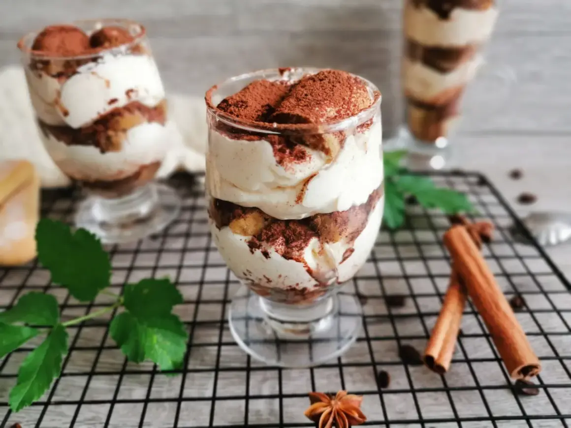 Pyszne tiramisu w pucharkach, warstwowo ułożone z kremem i biszkoptami, posypane kakao. Idealne na deser.