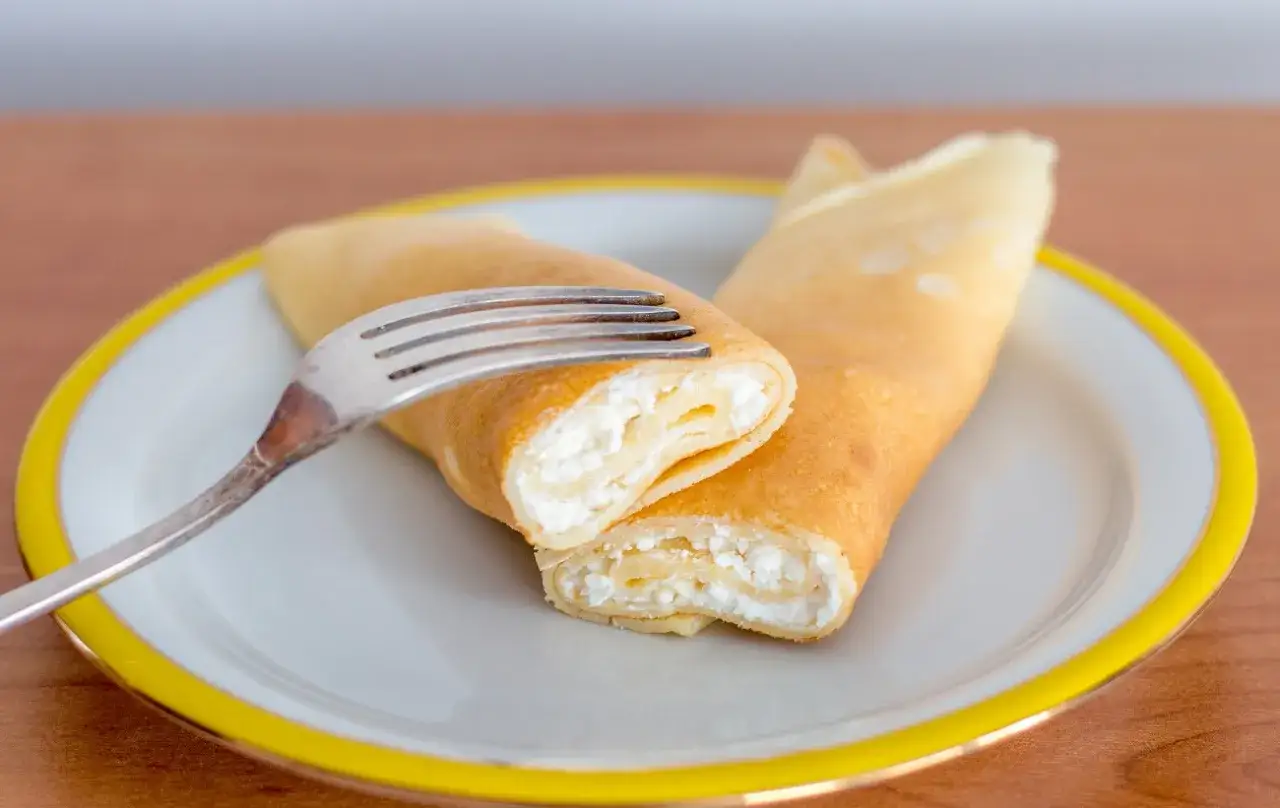 Dwa naleśniki z serem na talerzu, jeden przekrojony, widoczny puszysty ser.