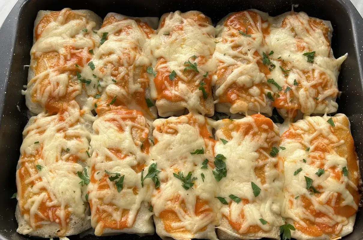 Zapiekane naleśniki z kurczakiem, polane sosem pomidorowym i posypane ciągnącym się serem, ozdobione natką pietruszki.