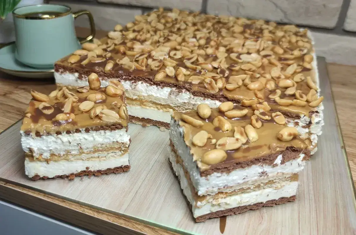 Pyszne ciasto snickers z warstwami kremu, karmelu i orzeszk&oacute;w ziemnych. Idealne na deser.