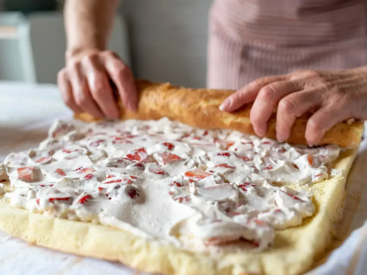Ręce zwijają biszkopt z kremem truskawkowym. Pyszna rolada biszkoptowa w przygotowaniu.
