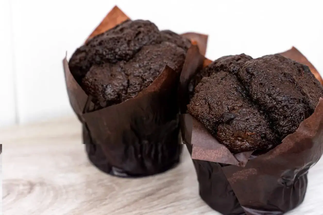 Dwa puszyste muffinki czekoladowe w brązowych papilotkach, gotowe do zjedzenia.