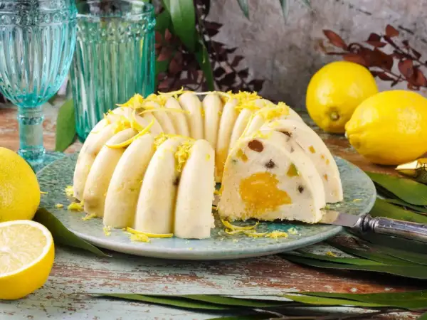 Pyszna babka z owocami, udekorowana skórką cytrynową, prezentuje się apetycznie na talerzu. Obok leżą świeże cytryny.