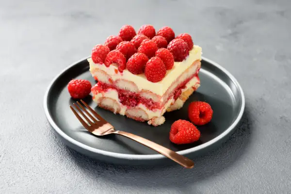 Pyszne tiramisu malinowe z warstwami biszkoptów, kremu i malin, ozdobione świeżymi malinami.