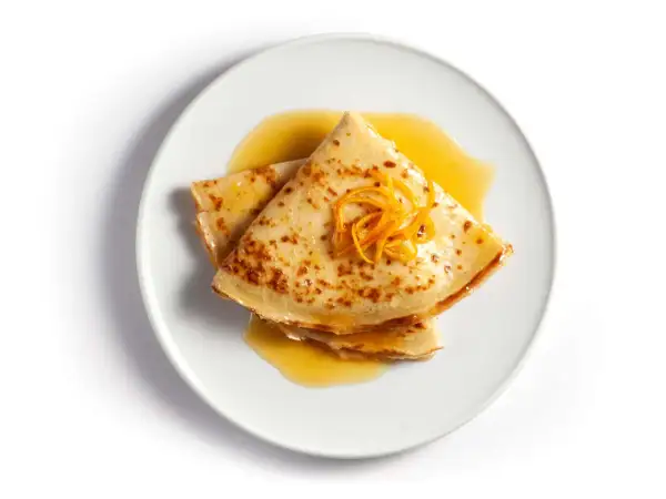 Złożone na pół naleśniki crepes suzette polane pomarańczowym sosem, ozdobione skórką pomarańczową.