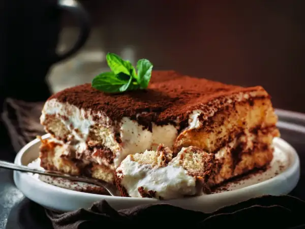 Pyszne tiramisu z mascarpone i śmietaną bez jajek, posypane kakao i ozdobione miętą. Idealne na deser.