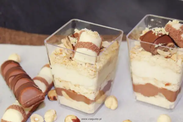 Pyszne deserki Kinder Bueno w pucharkach, warstwowo ułożone z kremem i czekoladą, posypane orzechami.