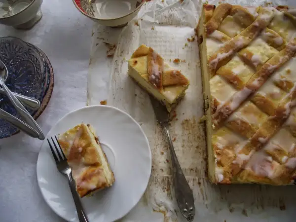 Pyszny sernik krakowski z kratką z ciasta i lukrem, jeden kawałek na talerzyku, gotowy do degustacji.