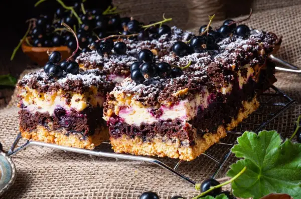 Pyszne ciasto skubaniec z czarną porzeczką i kremem, posypane cukrem pudrem i świeżymi owocami.